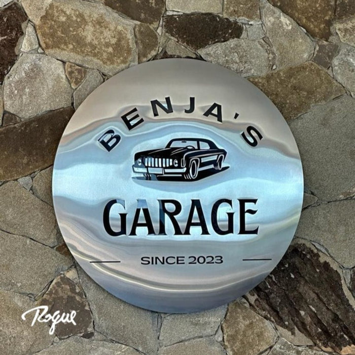 Benja's Garage: Placa circular em aço escovado com arte aplicada.
