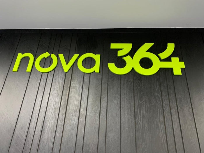 Nova 364: Letreiro em alto relevo na cor da marca, com recorte preciso sobre painel escuro.