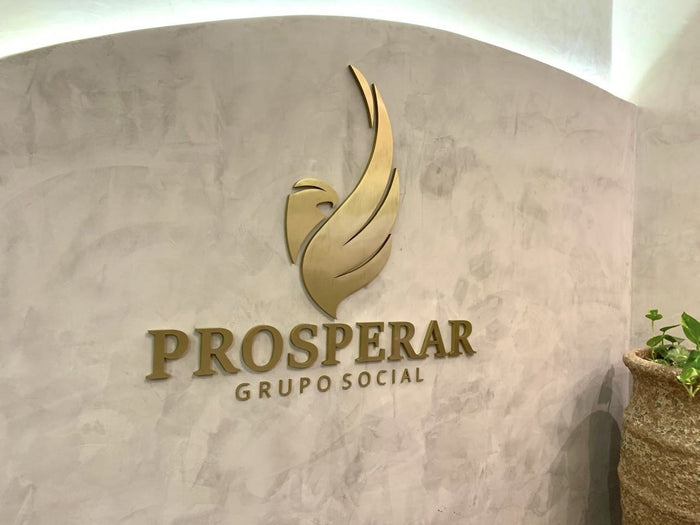 Prosperar Grupo Social: Símbolo e nome “Prosperar” montados em latão dourado, com “Grupo Social” em acrílico com face em latão dourado.
