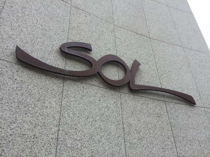 Sol: Letreiro em alto relevo de aço corten oxidado.