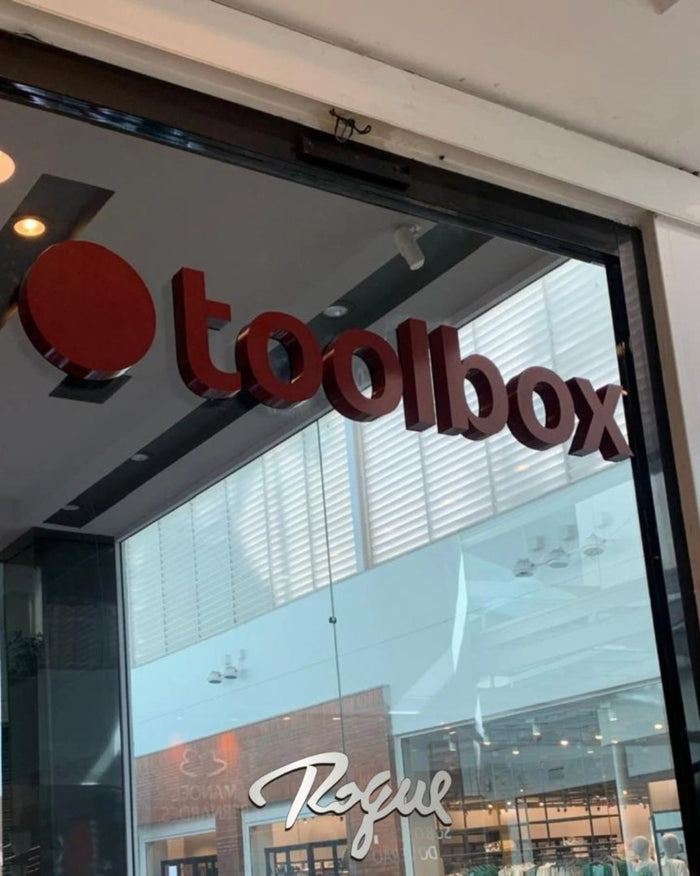 Toolbox: Letreiro em aço galvanizado com pintura vinho, em fachada de loja.